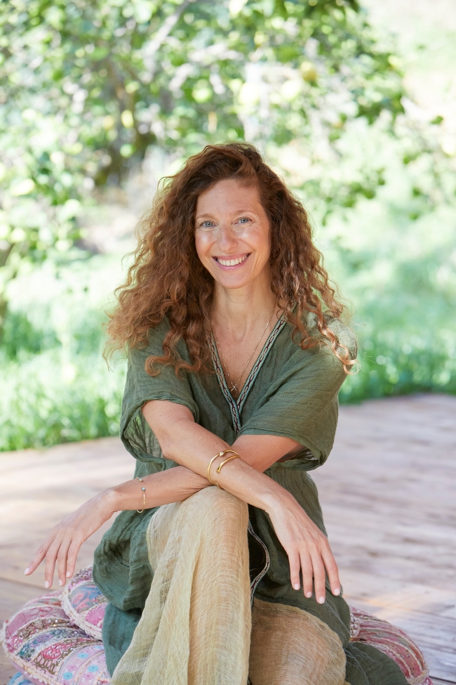 woman seated and smiling, in the background green vegetation