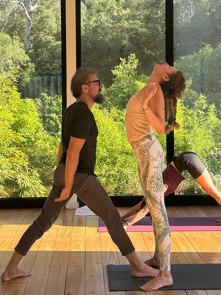 teacher assisting a yoga student to come up from a wheel pose. teacher facing student, student is looking up. forest in the background
